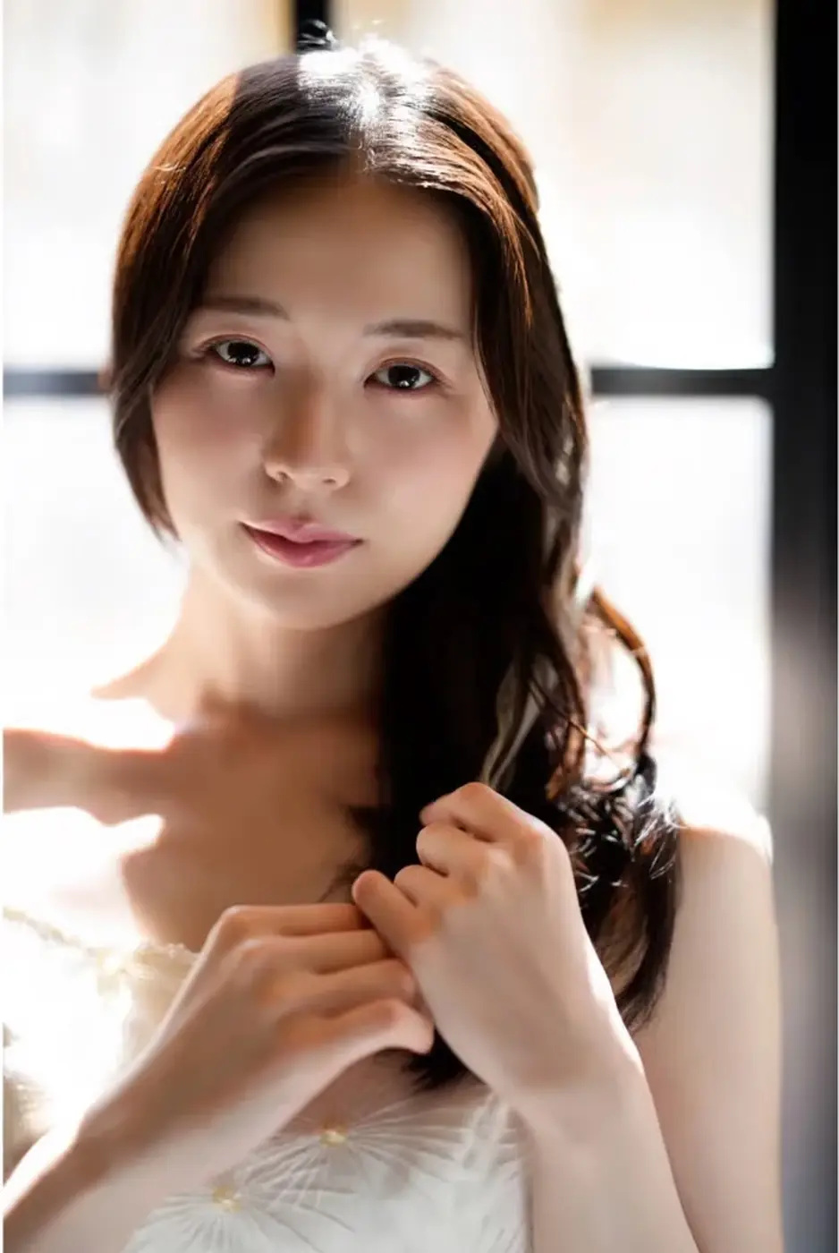 Close-up portrait of a dark-haired woman in soft backlight beside a window.