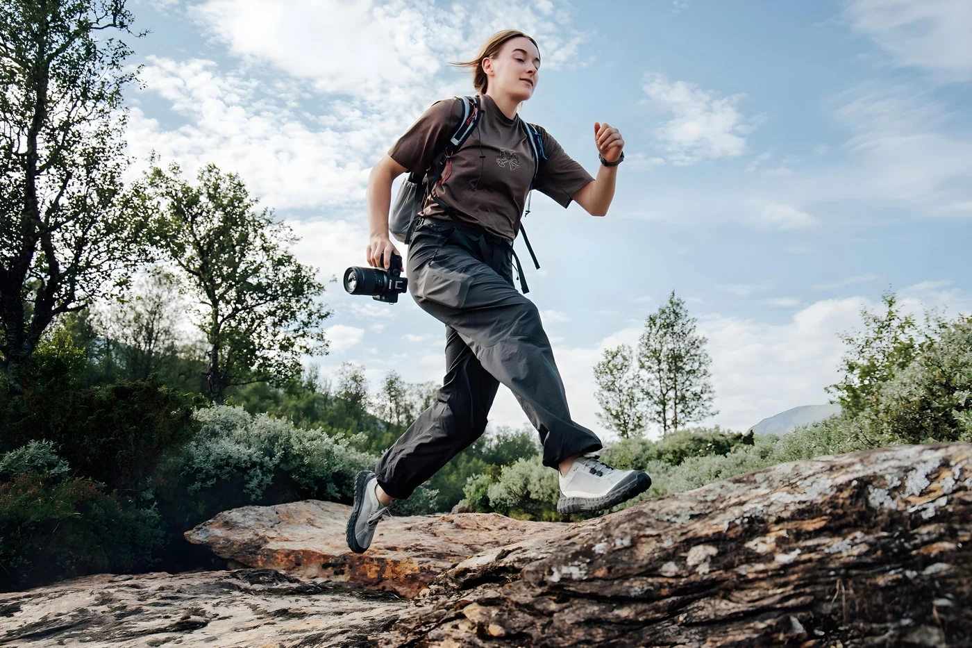 Fotograaf loopt met een Canon EOS R8 Mark II over rotsen in een groen landschap.