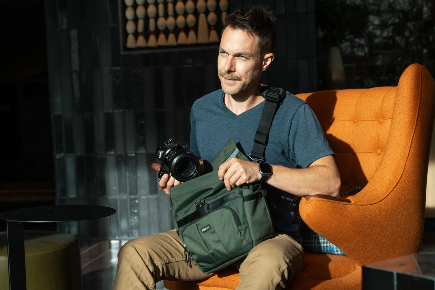Zittende fotograaf houdt een camera boven de geopende groene Think Tank FocusPoint Crossbody op zijn schoot.