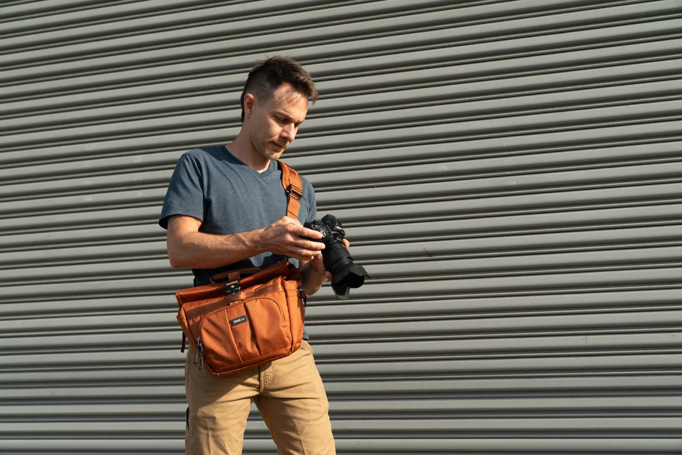Fotograaf met een roestkleurige Think Tank FocusPoint Crossbody schuin over zijn lichaam en een camera in zijn handen.