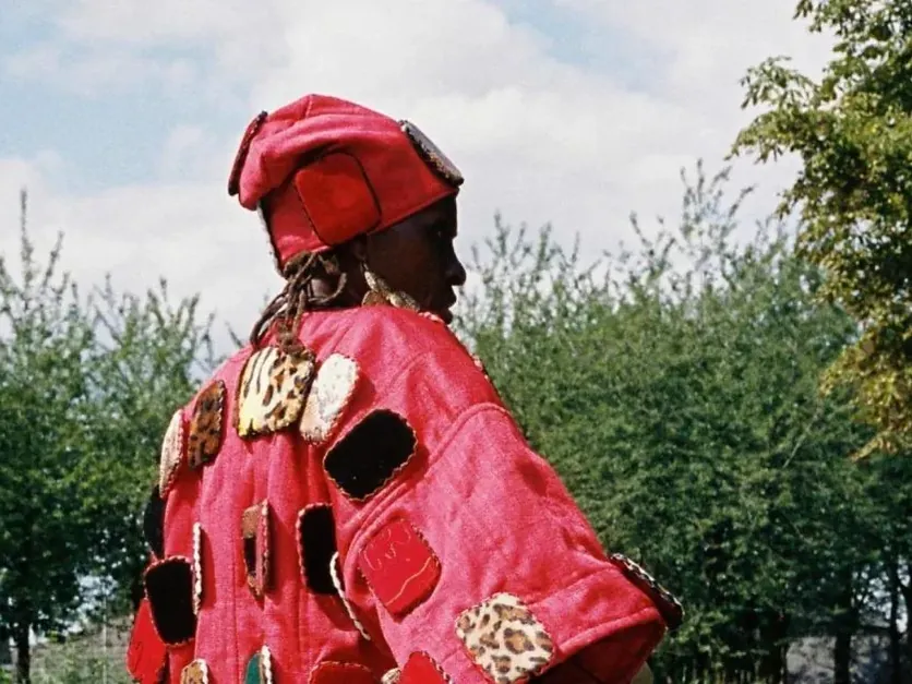 Persoon in een rode hoed en een met patronen versierde rode cape, gefotografeerd door Vincen Beeckman voor Parade.