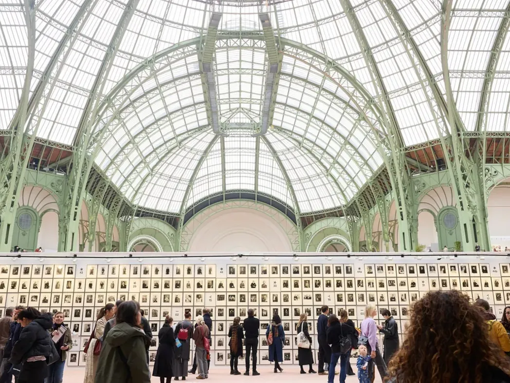 Bezoekers bekijken een wand met fotografische portretten tijdens een eerdere editie van Paris Photo onder het glazen dak van het Grand Palais.