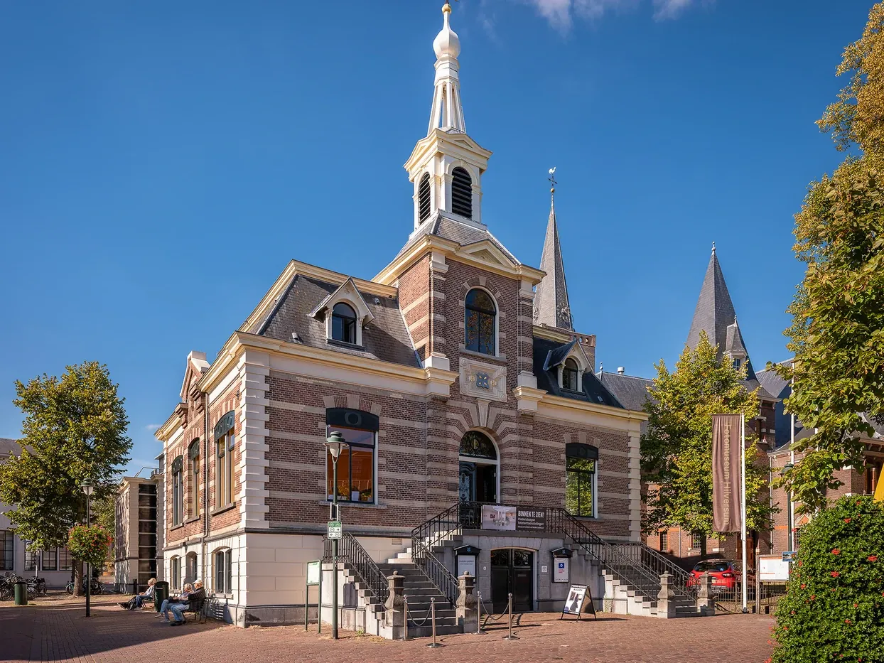 Bakstenen gebouw van Fotomuseum Hilversum op een zonnig plein onder blauwe lucht, met een banner naast de trap.