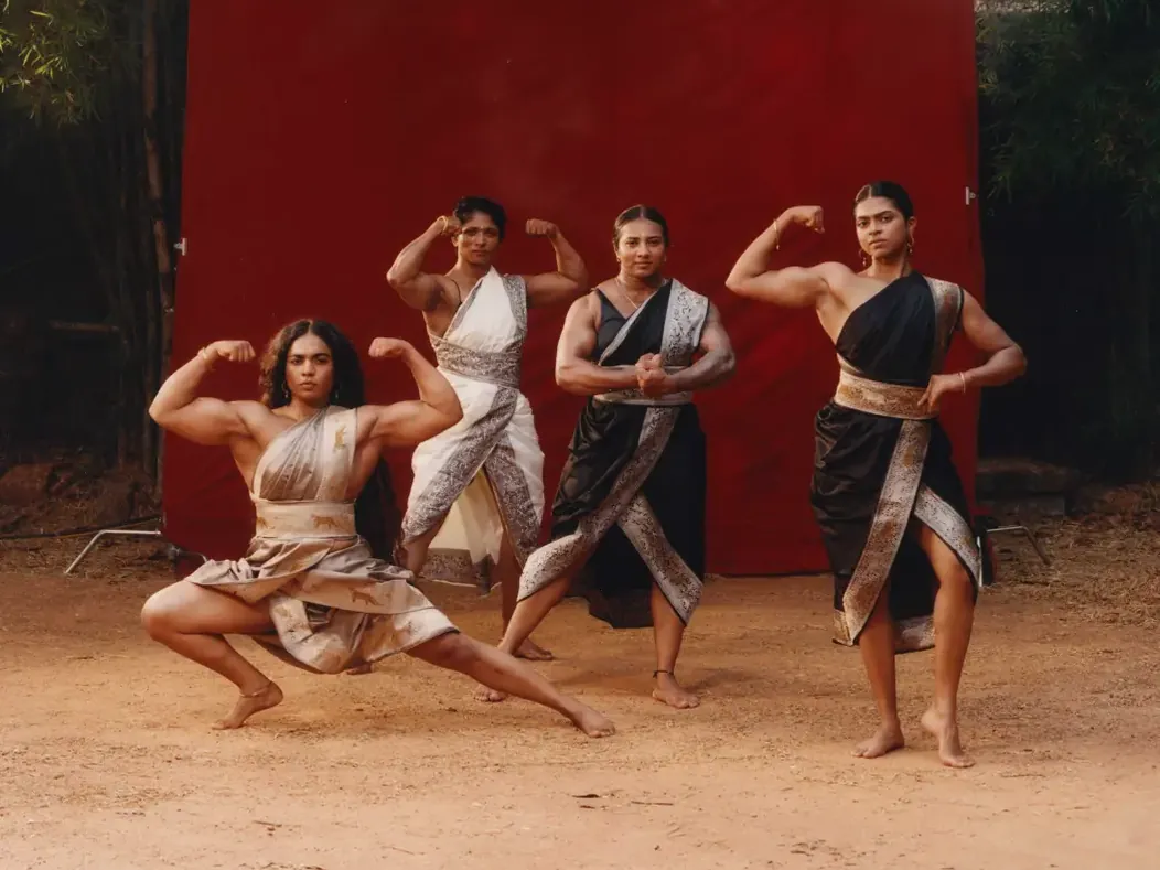 Vier vrouwelijke bodybuilders poseren voor een rood decor in werk van Keerthana Kunnath.