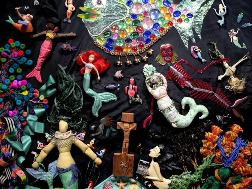 Kleurrijke collage met een grote vis, zeemeerminnen, poppen, schelpen en andere fantasiefiguren op een roze en zwarte achtergrond.