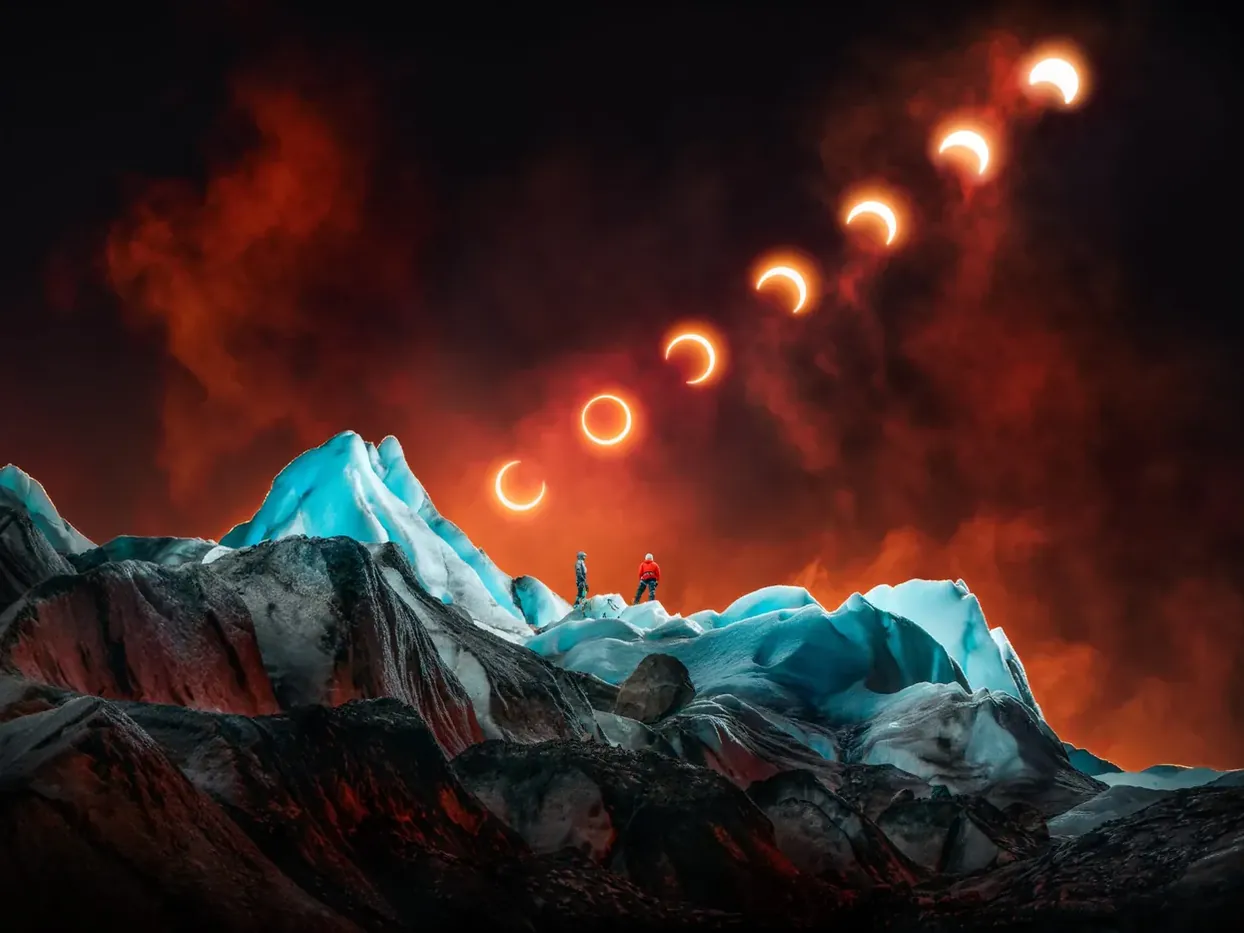 Twee klimmers op blauw verlicht gletsjerijs, met opeenvolgende fasen van een zonsverduistering boven een rood-oranje lucht.