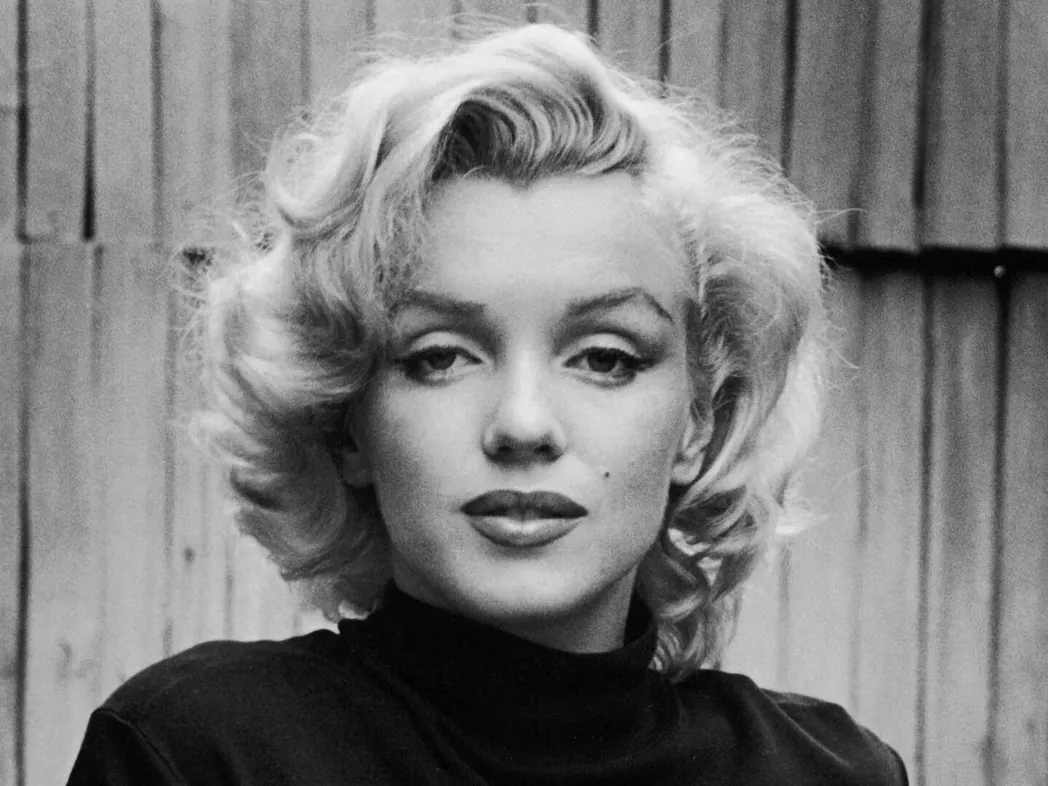 Zwart-witportret van Marilyn Monroe met blond haar voor een houten achtergrond.