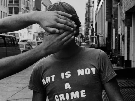 Zwart-witfoto van een jongen in een straat met het T-shirt ‘ART IS NOT A CRIME’, terwijl twee handen zijn gezicht bedekken.