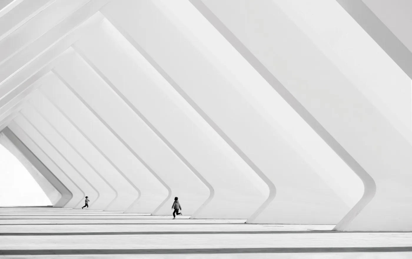 Black-and-white photograph of two small figures among large white architectural ribs and long shadows, by Nina Papiorek.