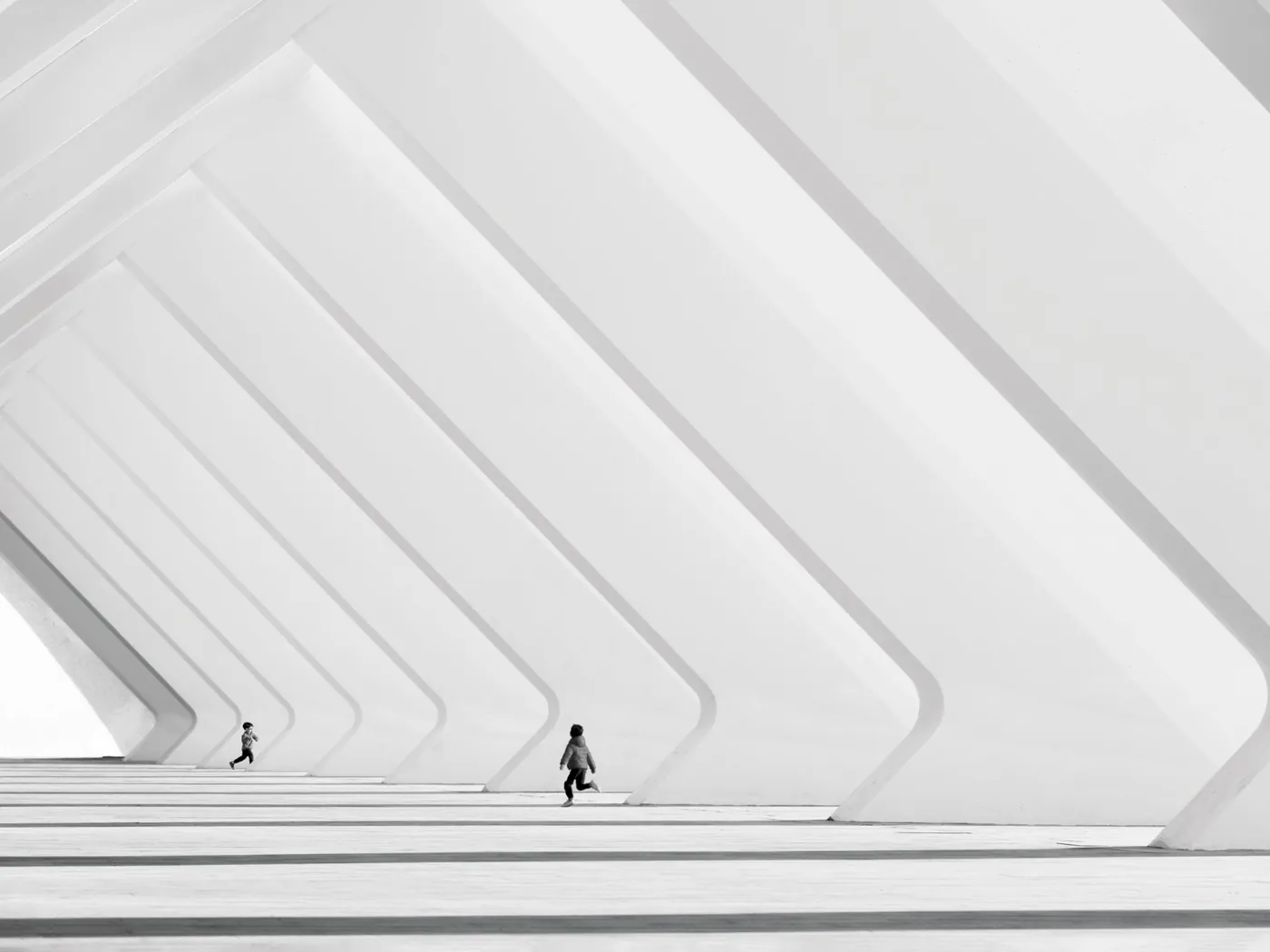 Zwart-witfoto van twee kleine figuren tussen grote witte architectonische ribben en lange schaduwen, door Nina Papiorek.