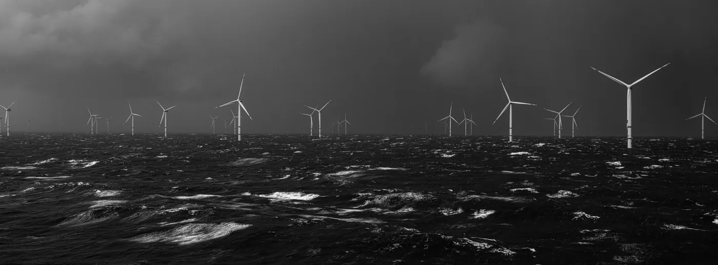 Black-and-white photograph of wind turbines on a choppy sea beneath dark clouds, by Kadir van Lohuizen.