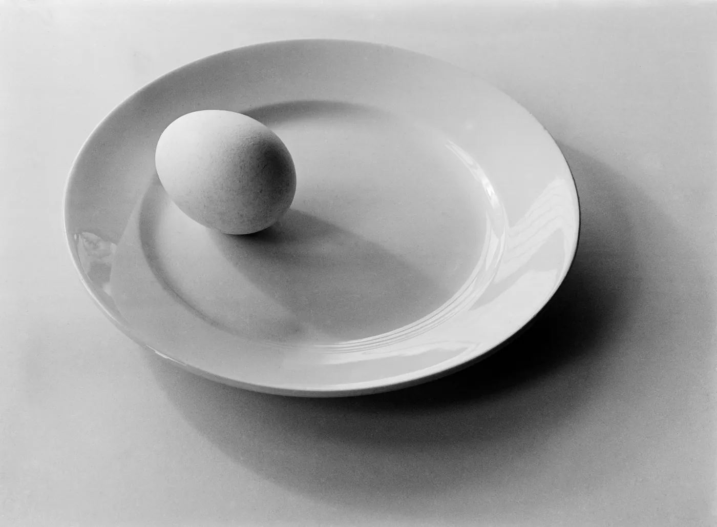 Black-and-white still life of an egg on a white plate with shadows, photographed by Violette Cornelius in Amsterdam, 1939.