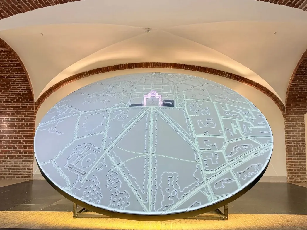 Een grote ronde, verlichte installatie in een binnenruimte met bakstenen gewelven.