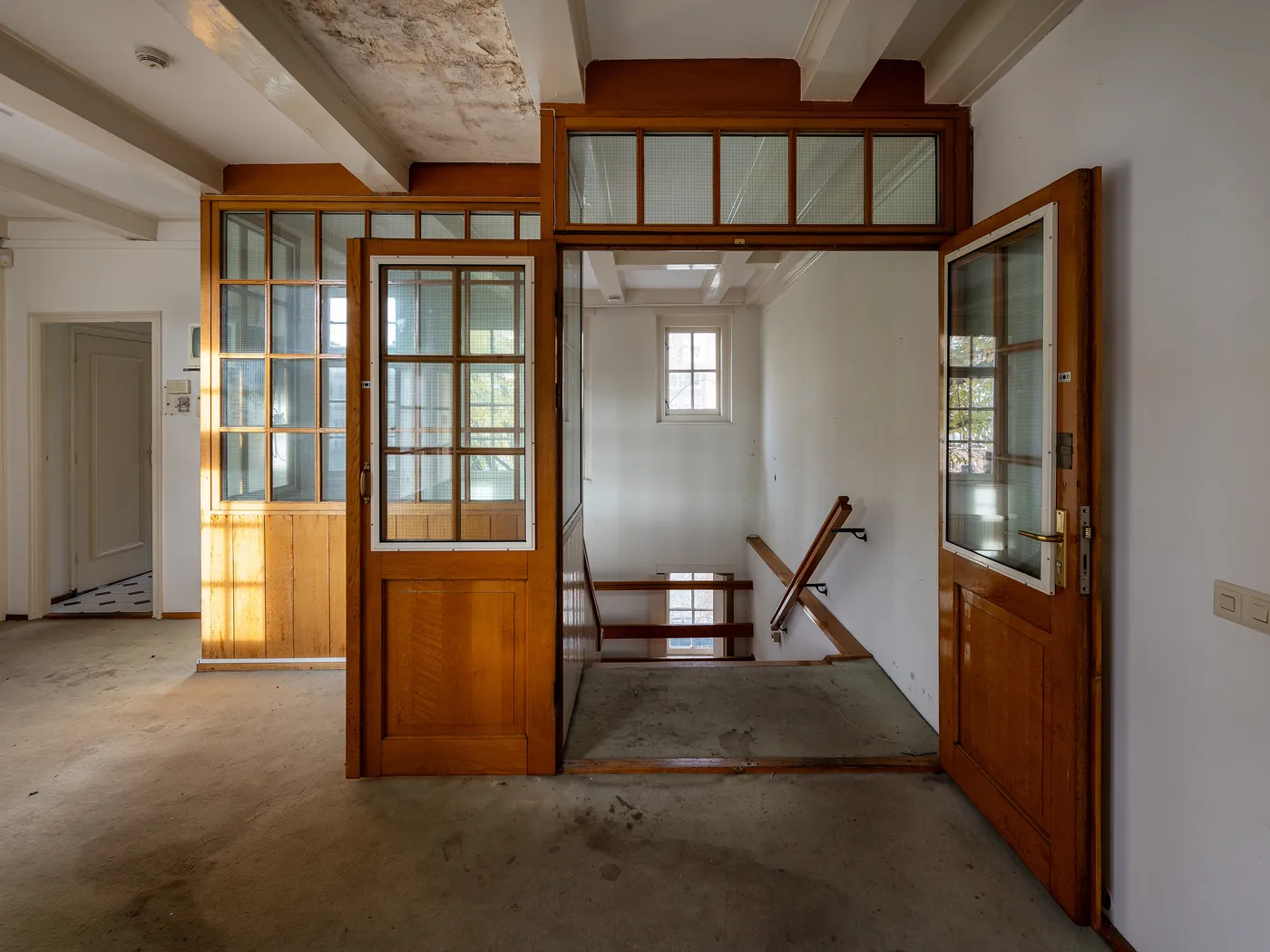 Houten deuren met glas en een trappenhuis in het lege Walenweeshuis, gefotografeerd door Roos Aldershoff.