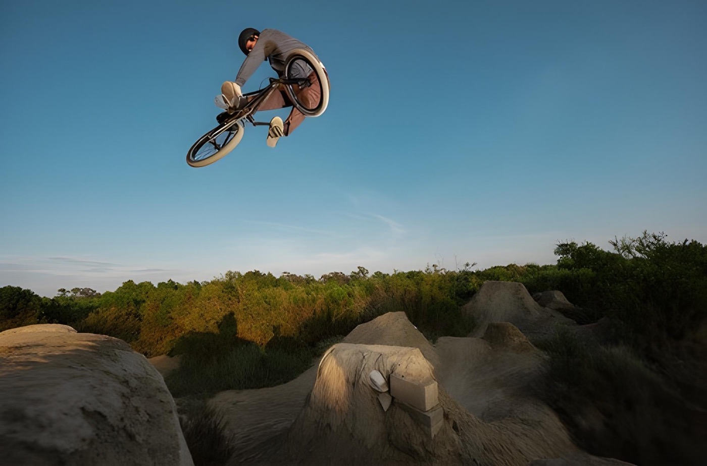 BMX-rijder springt boven een zandbaan tegen een blauwe lucht