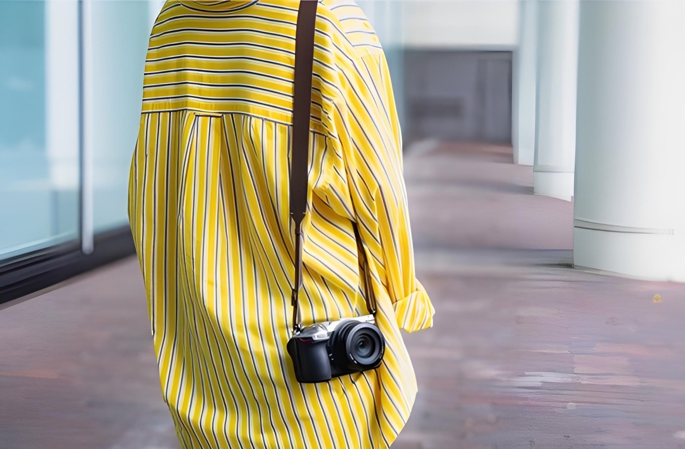 Zilveren Nikon Z5IIC aan een schouderriem bij een geel gestreept overhemd