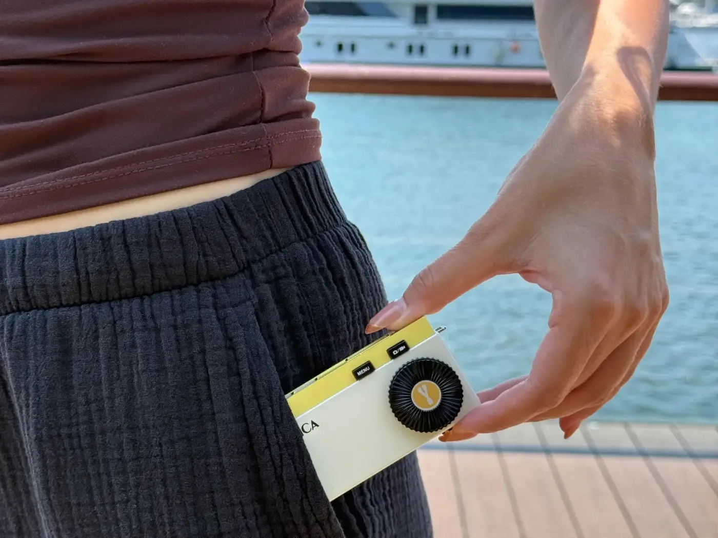 Vrouw steekt een wit-gele Yashica Y16 Pocket Camera in haar broekzak