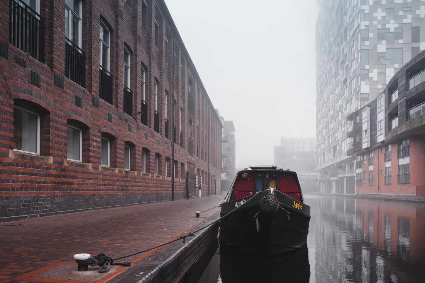 Misty view of a quiet canal with a boat and brick buildings in Birmingham, UK.