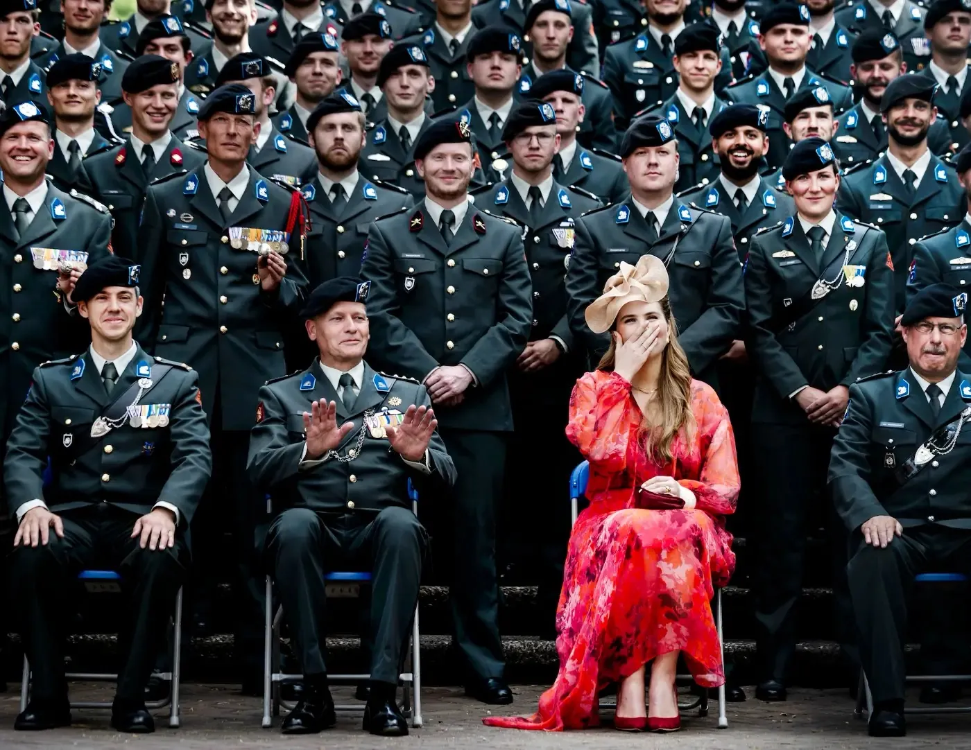Princess Amalia in a pink and red dress among military personnel in uniform, photographed by Remko de Waal
