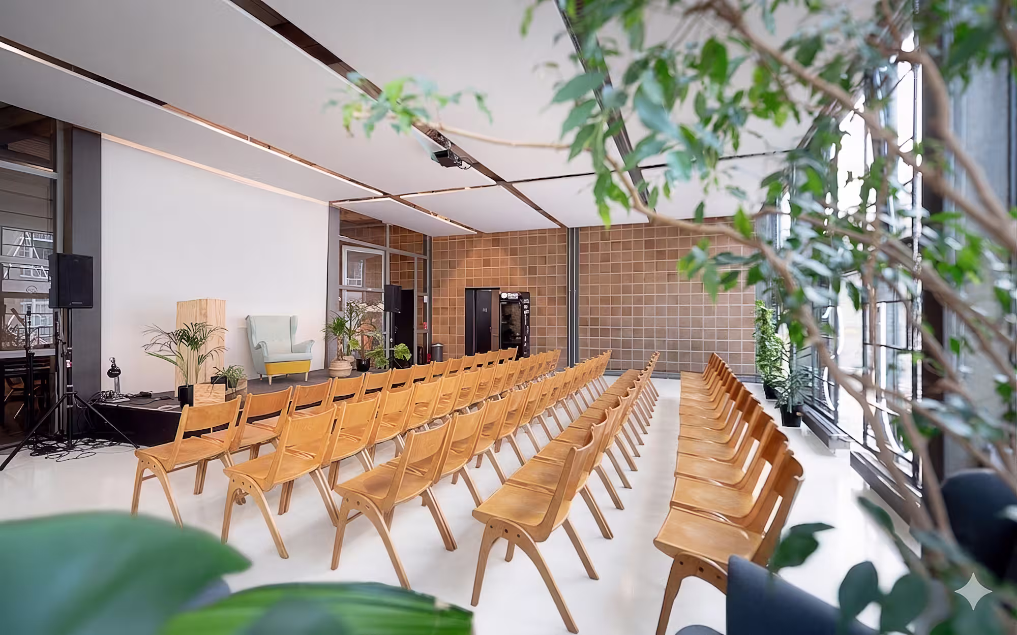 Modern event space at betahaus with wooden chairs in rows, a stage, plants, and large windows with natural light.