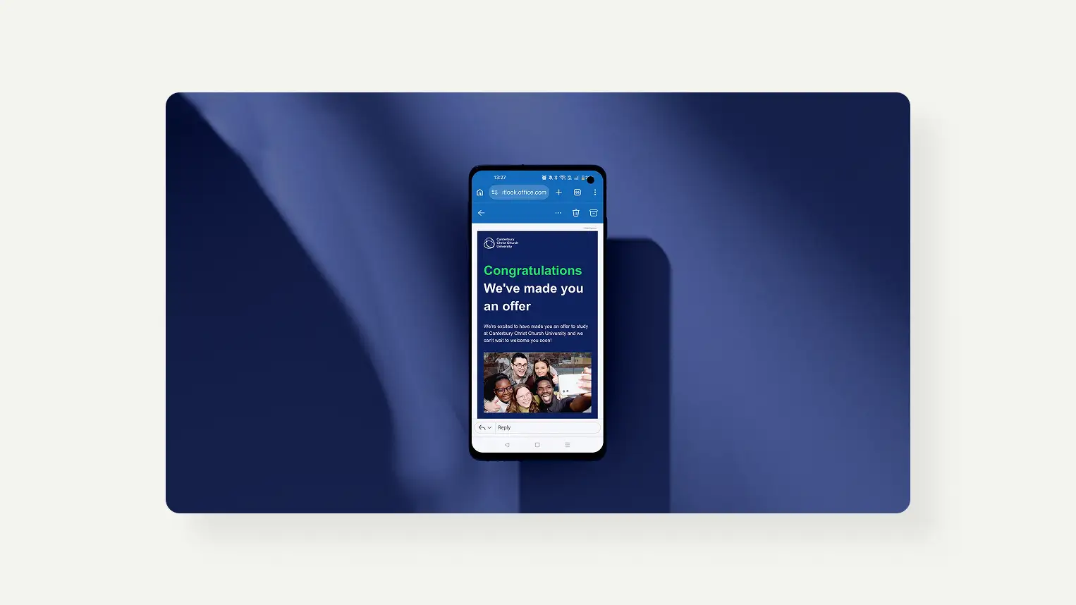 Smartphone displaying an email with the message 'Congratulations We've made you an offer' from Canterbury Christ Church University and a photo of five smiling people taking a selfie.