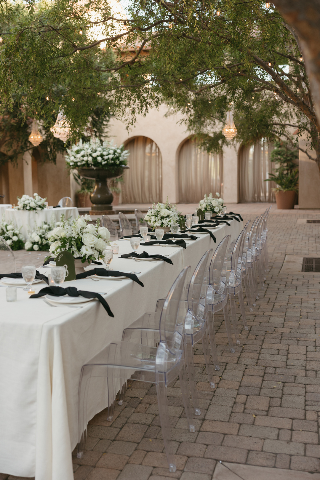 A modern meets romantic reception featuring white flowers and black and green details is set in the Serra Plaza Courtyard.