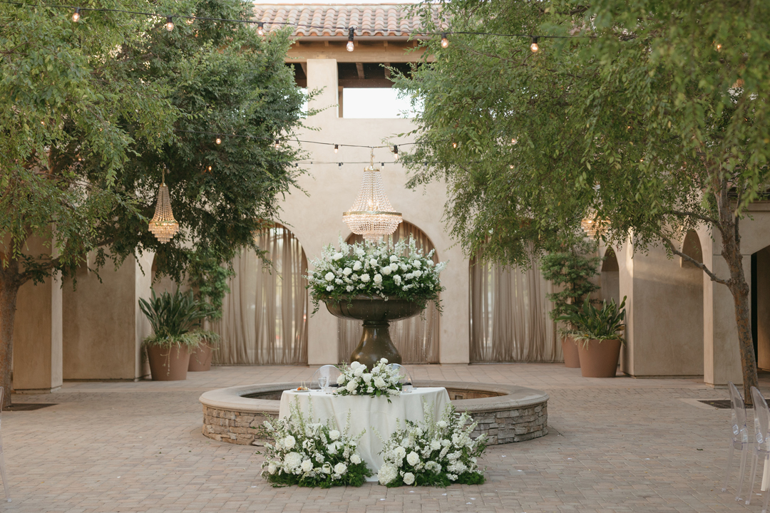 White florals and greenery decorate the bride and groom's sweetheart table in the Serra Plaza Courtyard.