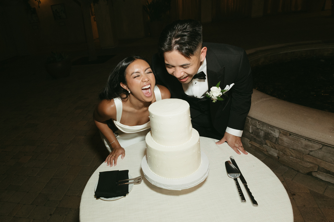 Bride and groom pose taking a bite out of their wedding cake.