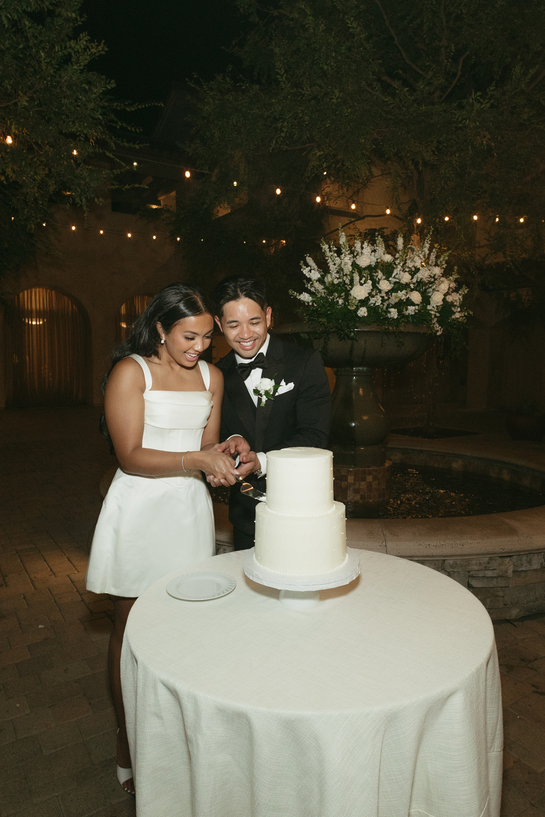 Bride and groom excitedly cut 2-tier wedding cake.