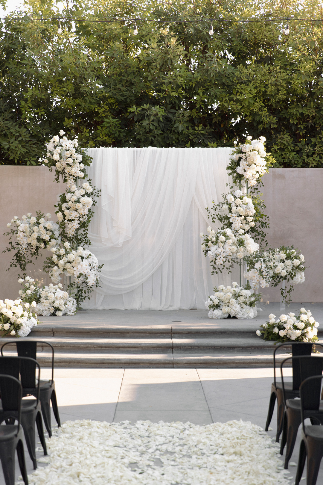 White wedding ceremony backdrop with draped fabric and white flowers.