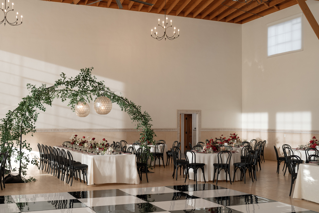 Best indoor wedding venue hosts romantic wedding reception complete with greenery, globe pendant lights, wooden table numbers, taupe candlesticks, and custom printed menu details.