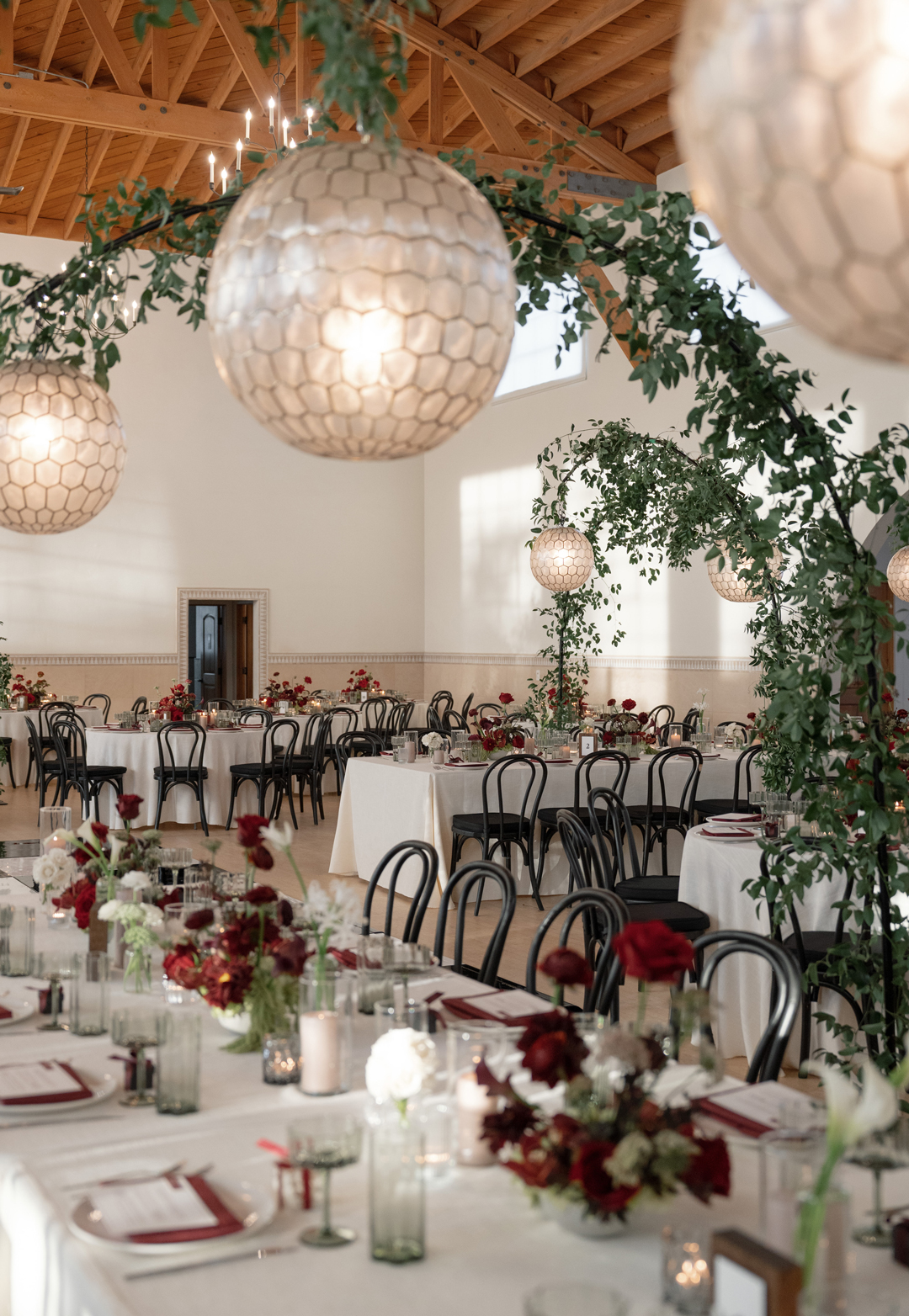 Romantic red wedding reception decor tops tables and greenery hangs above.