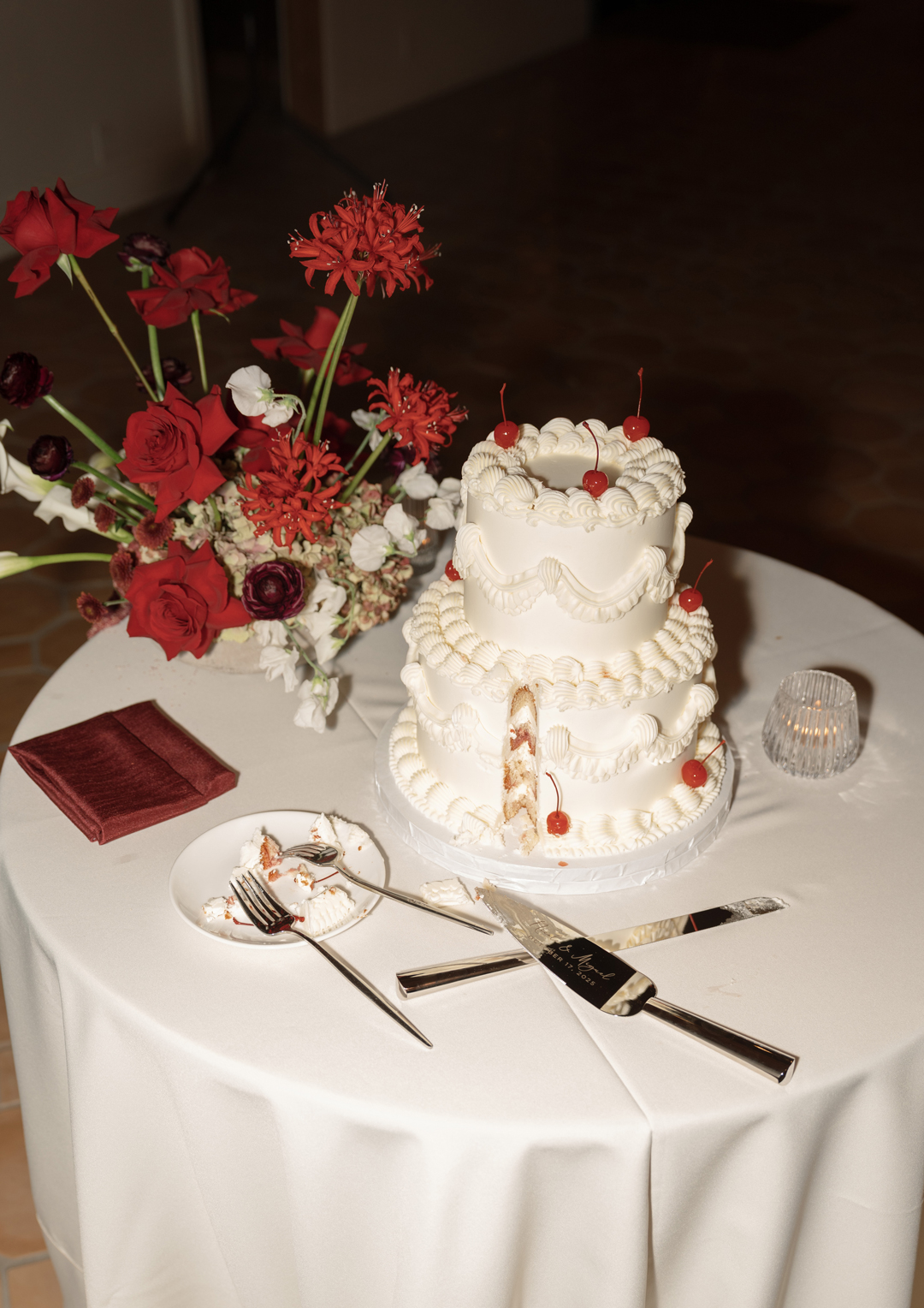 Cake table with vintage wedding cake with cherry details decorated with red flowers.