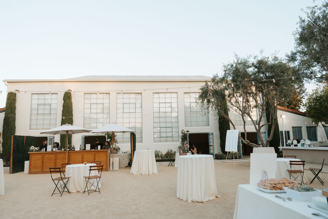 Cocktail tables are set outside in the courtyard where olive trees surround the wedding venue.