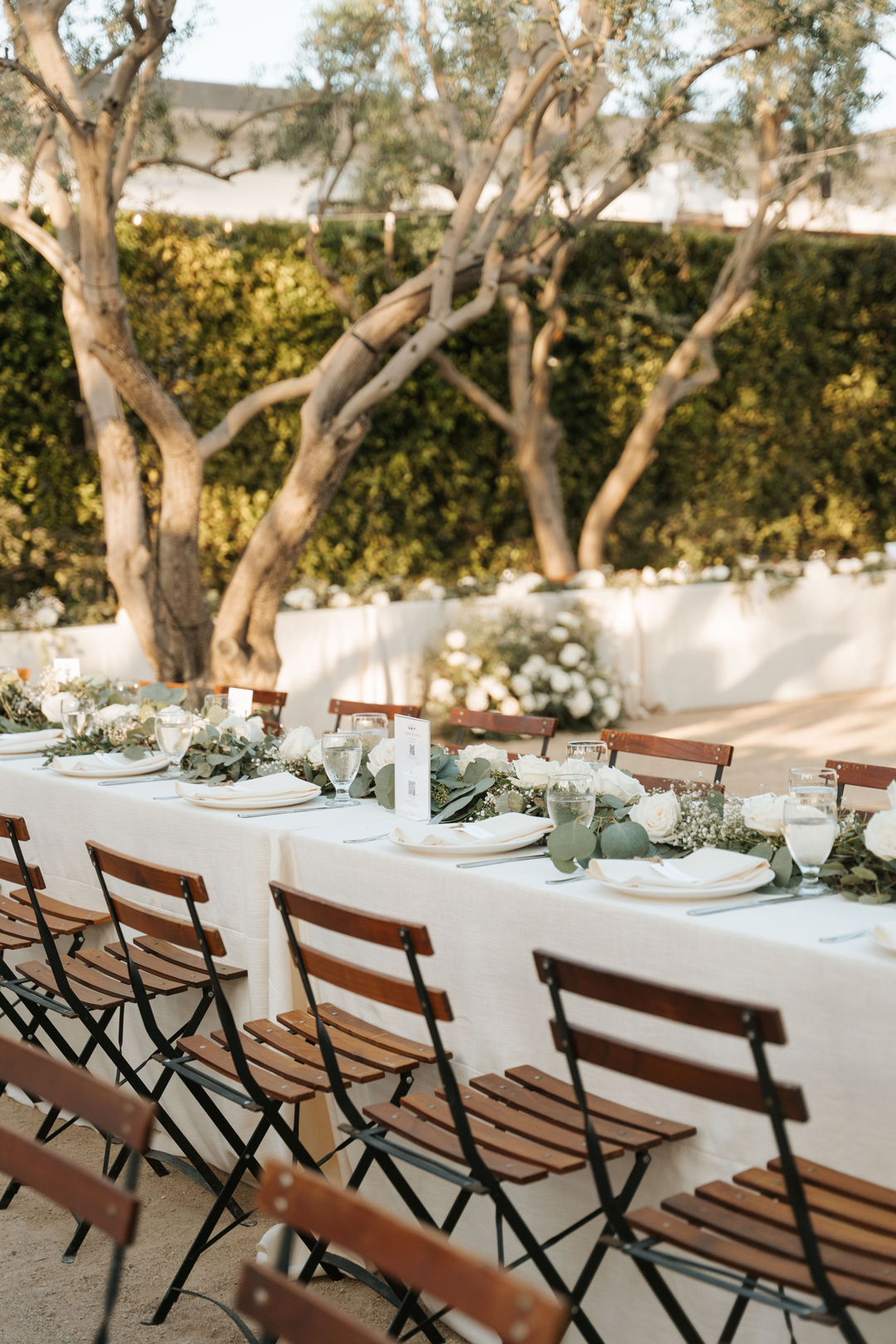 Eucalyptus and white flowers decorate wedding reception tables outside in the Olive Grove.