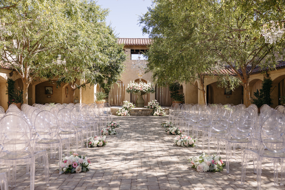 Pastel pink and white flowers line the aisle for an outdoor courtyard wedding in Orange County.