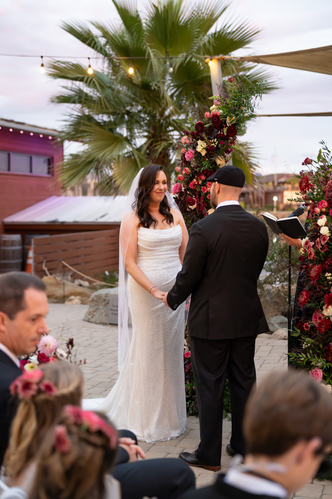 Bride and groom share vows with floral arch framing them in.