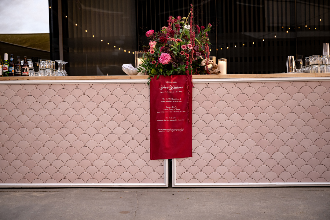 Wedding bar with pink scallop details and burgundy fabric cocktail sign.
