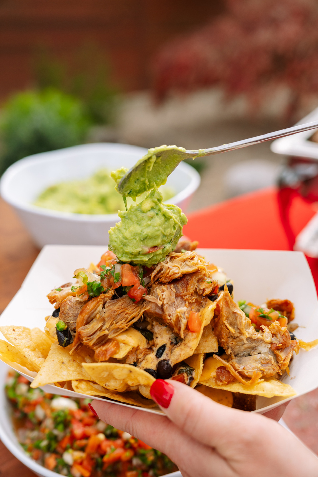 Loaded carnitas nachos being topped with guacamole for the big game.