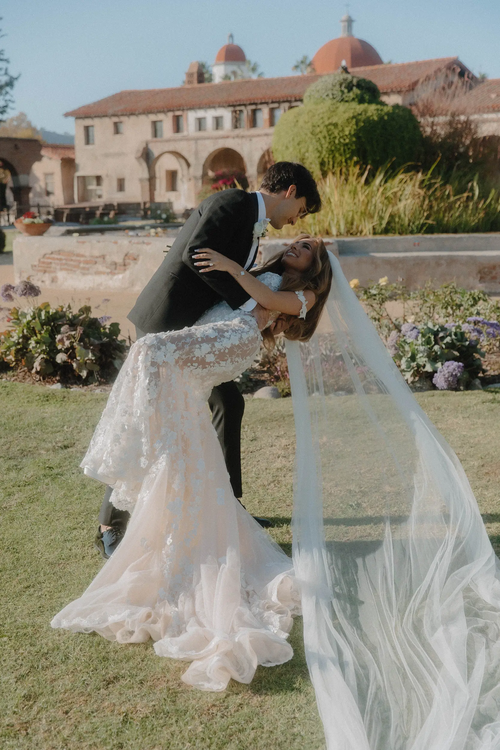 Groom dips bride for a kiss with Mission San Juan Capistrano as the backdrop.
