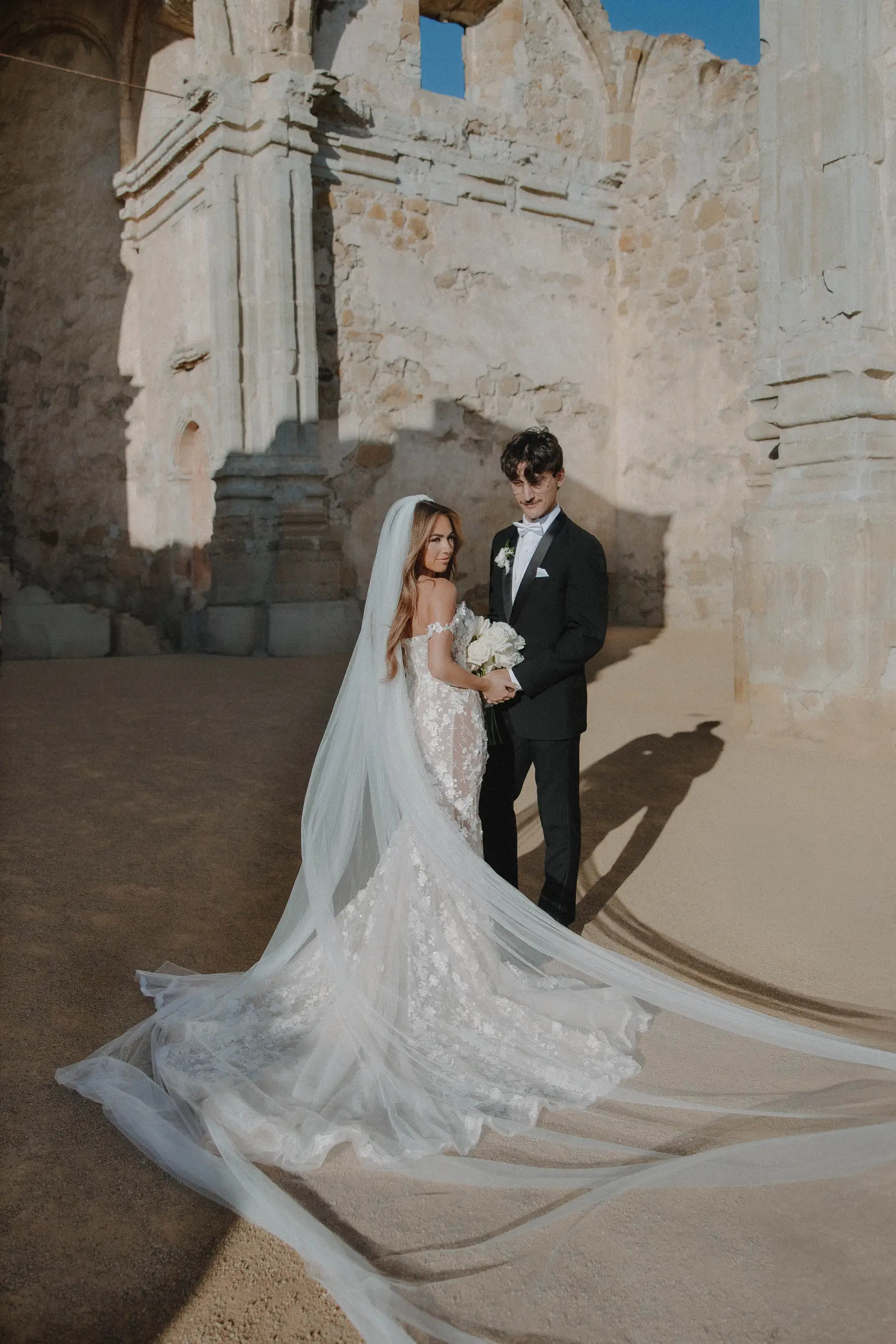 Bride and groom pose at Mission San Juan Capistrano for their wedding portraits.