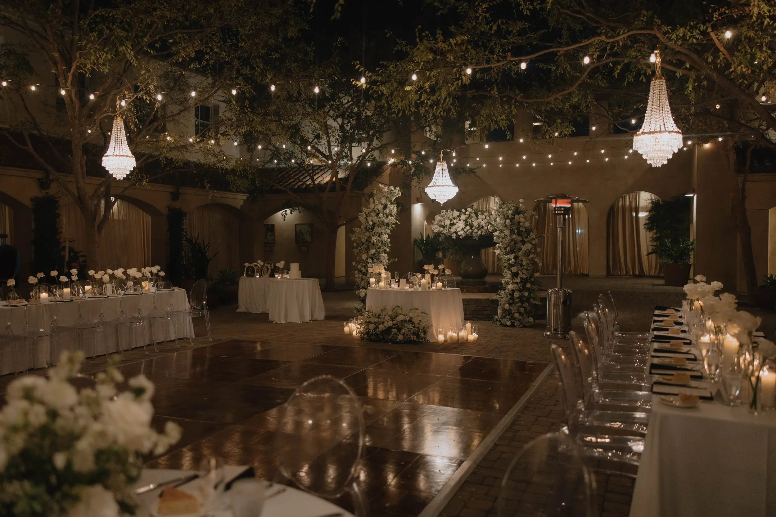 Romantic outdoor wedding reception in the Serra Plaza Courtyard with candles, chandeliers, and white roses.