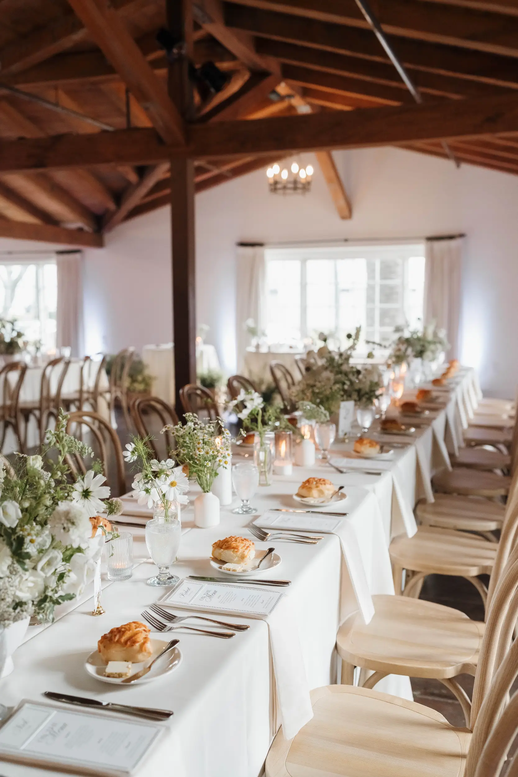 White flowers and greenery top tables inside the West Wing for a boho wedding reception.