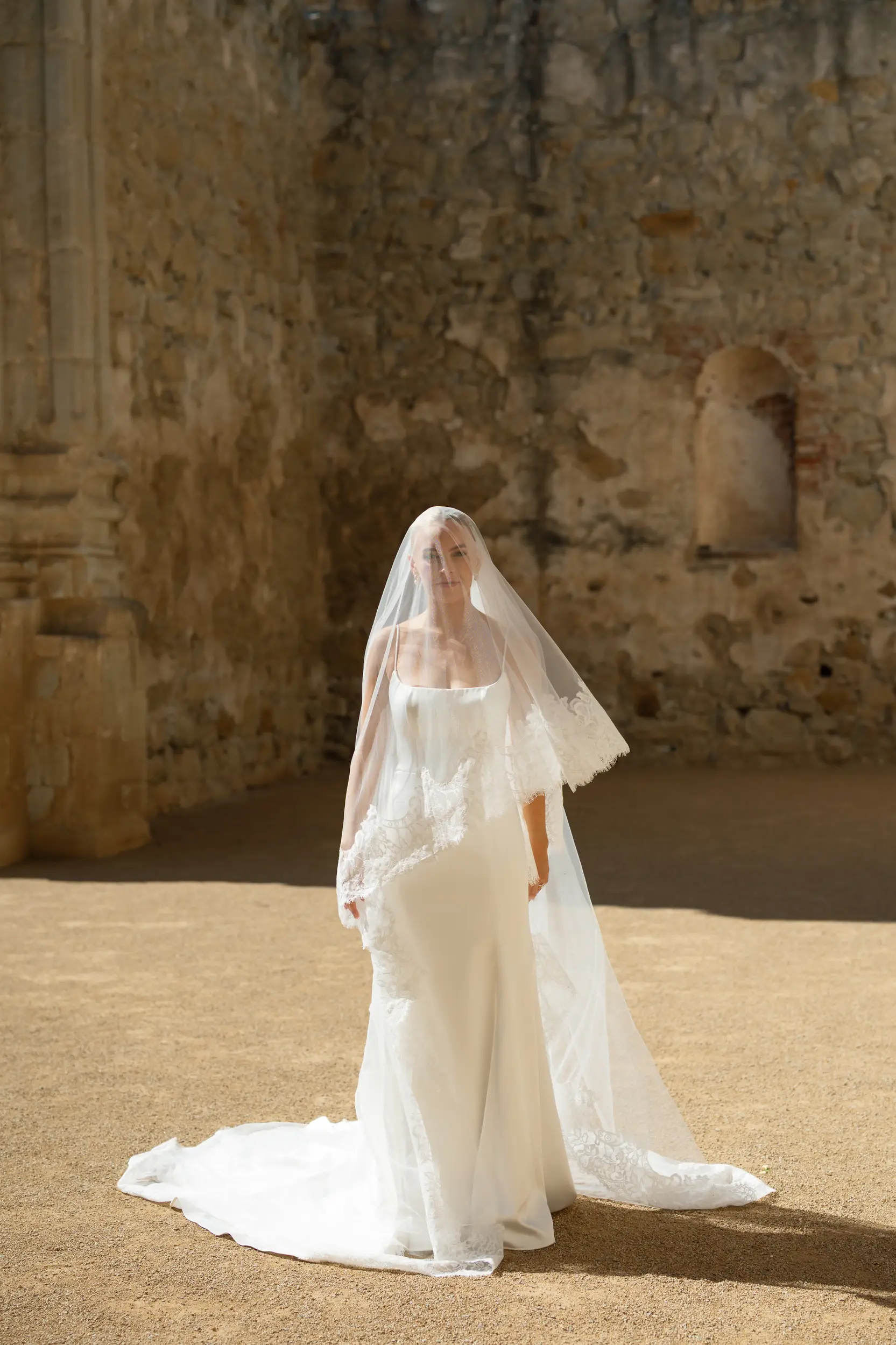 Bride standing with veil draped over face at Mission San Juan Capistrano.