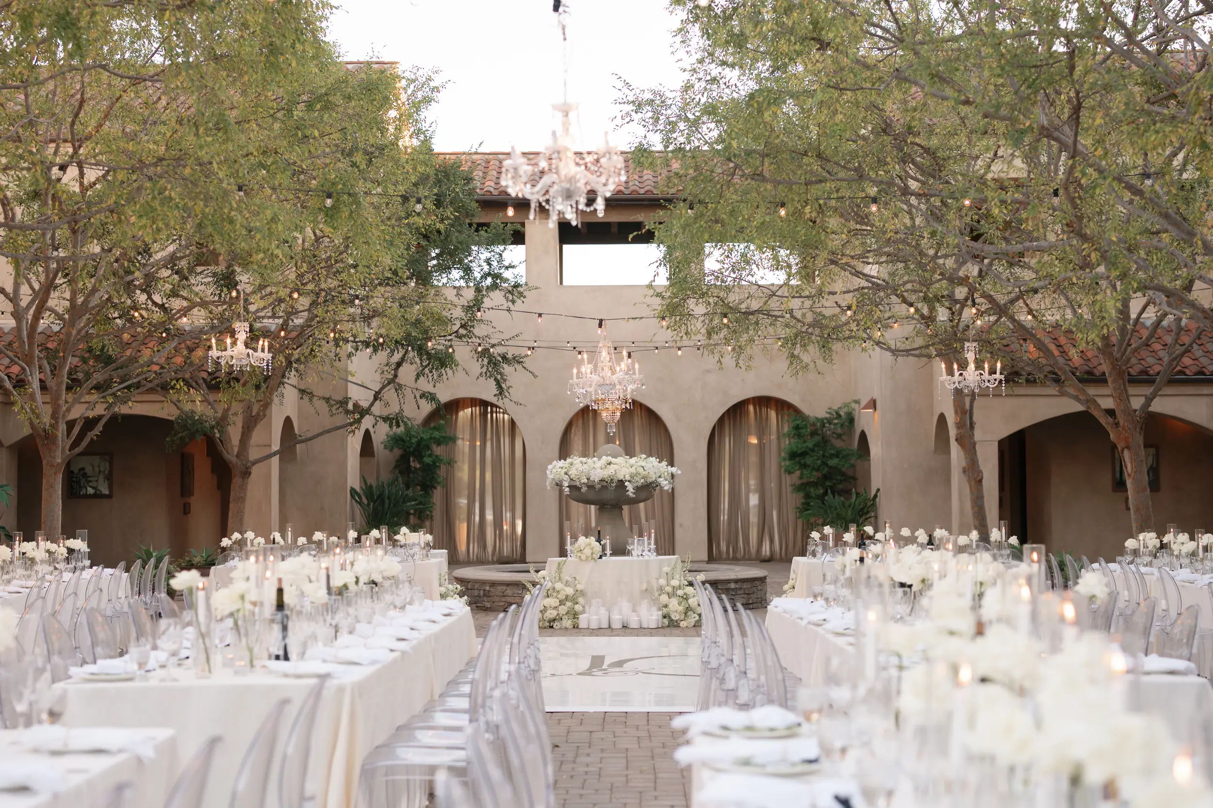 White floral wedding reception with green trees framing the space in.