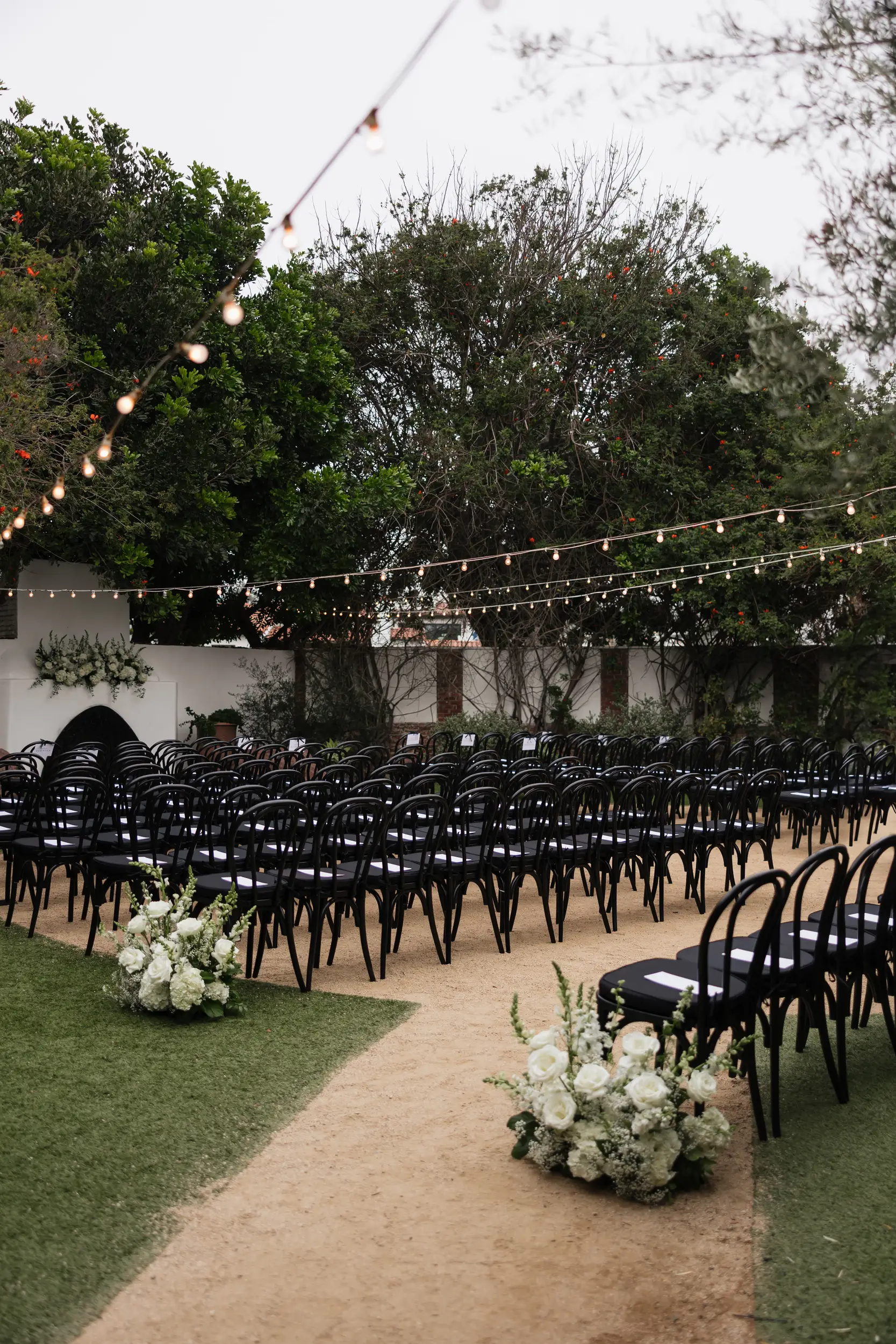 White flowers decorate the courtyard and black chairs are set for an outdoor wedding ceremony.