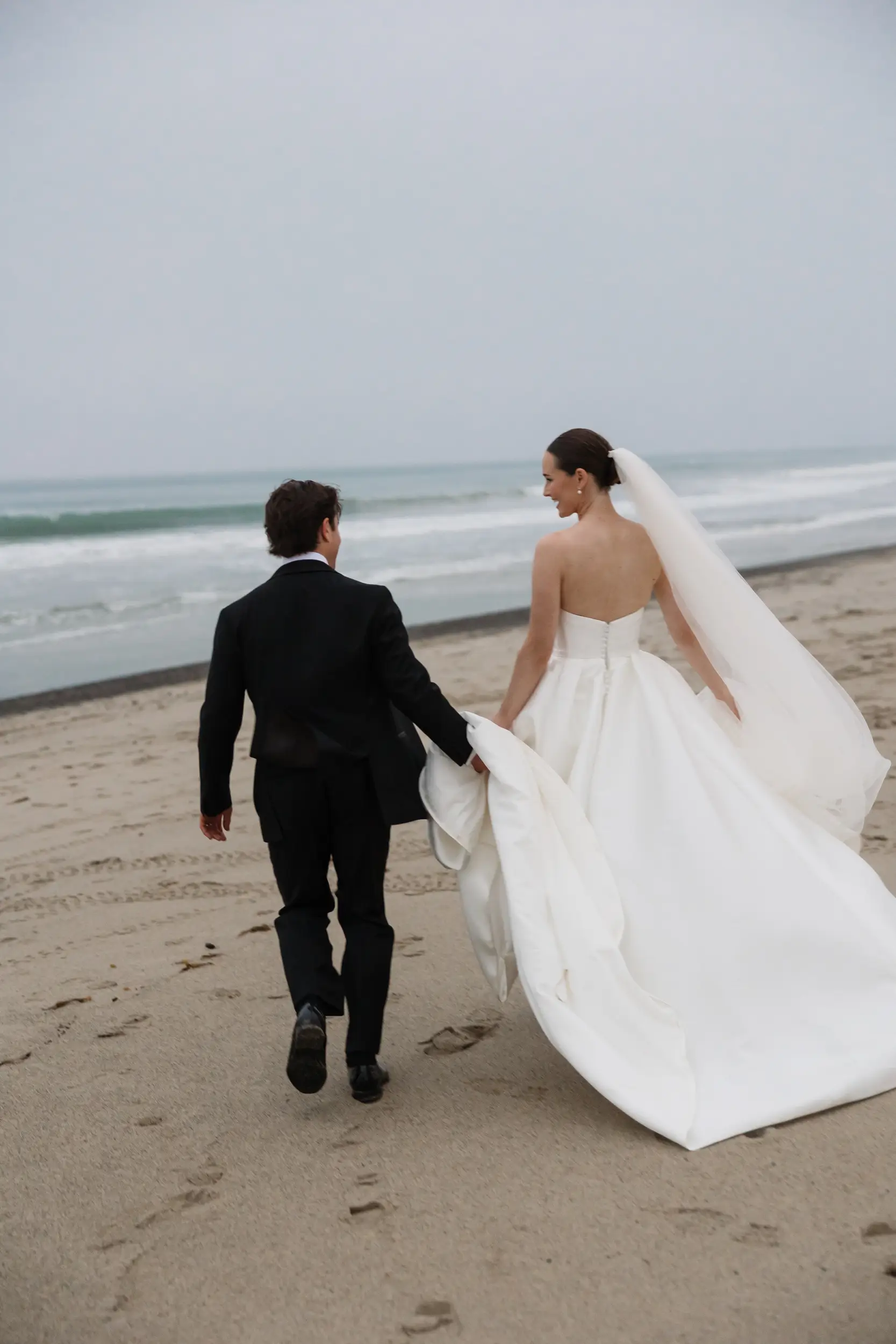 Bride and groom walk towards the ocean on the beach for romantics.