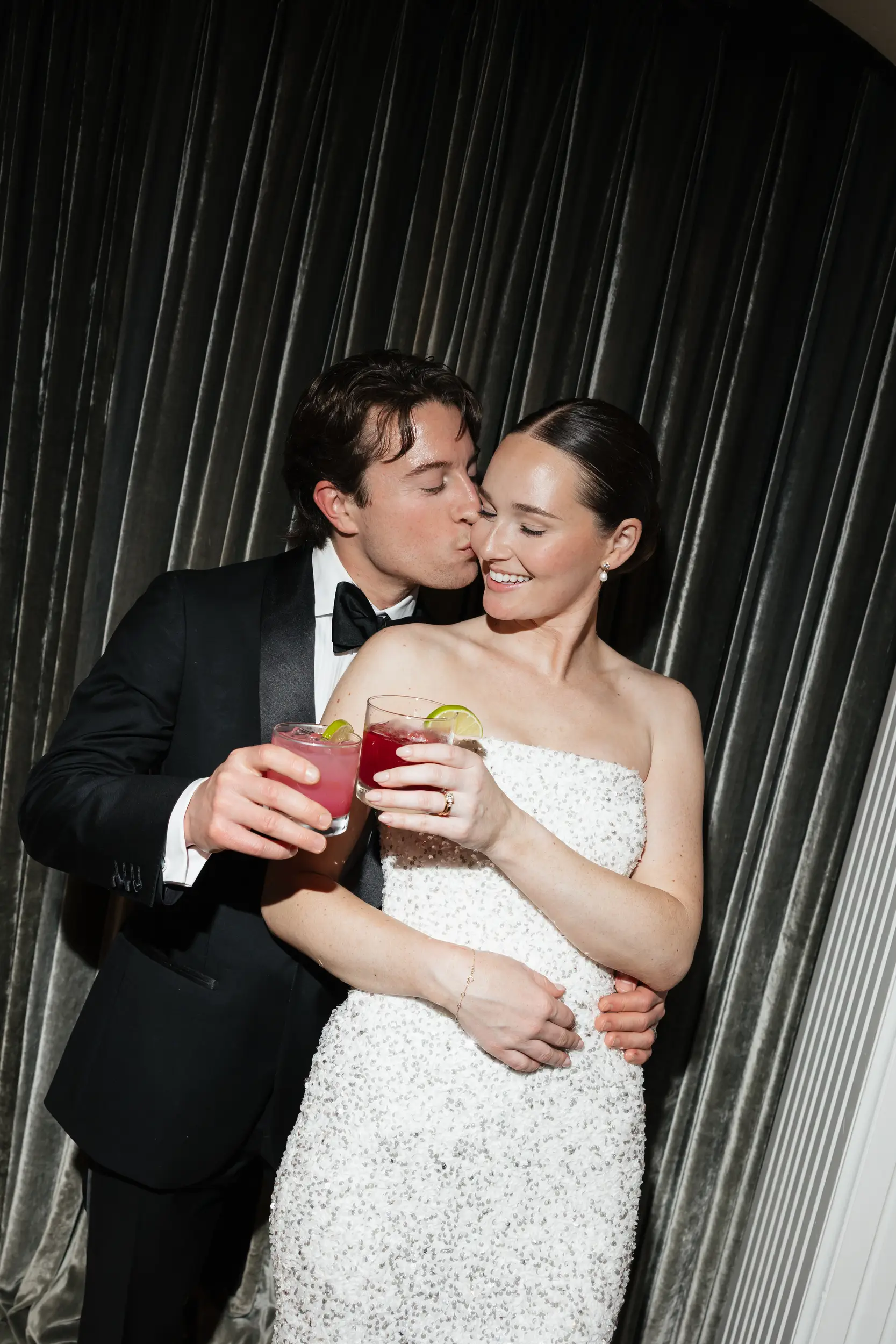Bride and groom share a kiss with cocktails in hand.