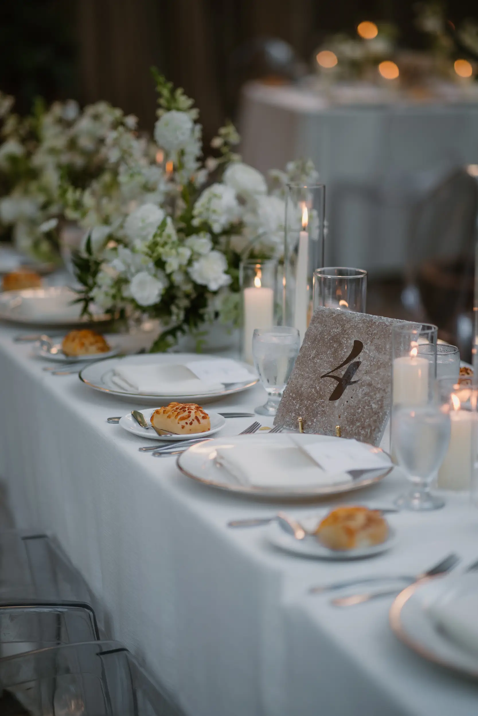 Wedding reception tablescape with stone table numbers and white floral centerpieces.
