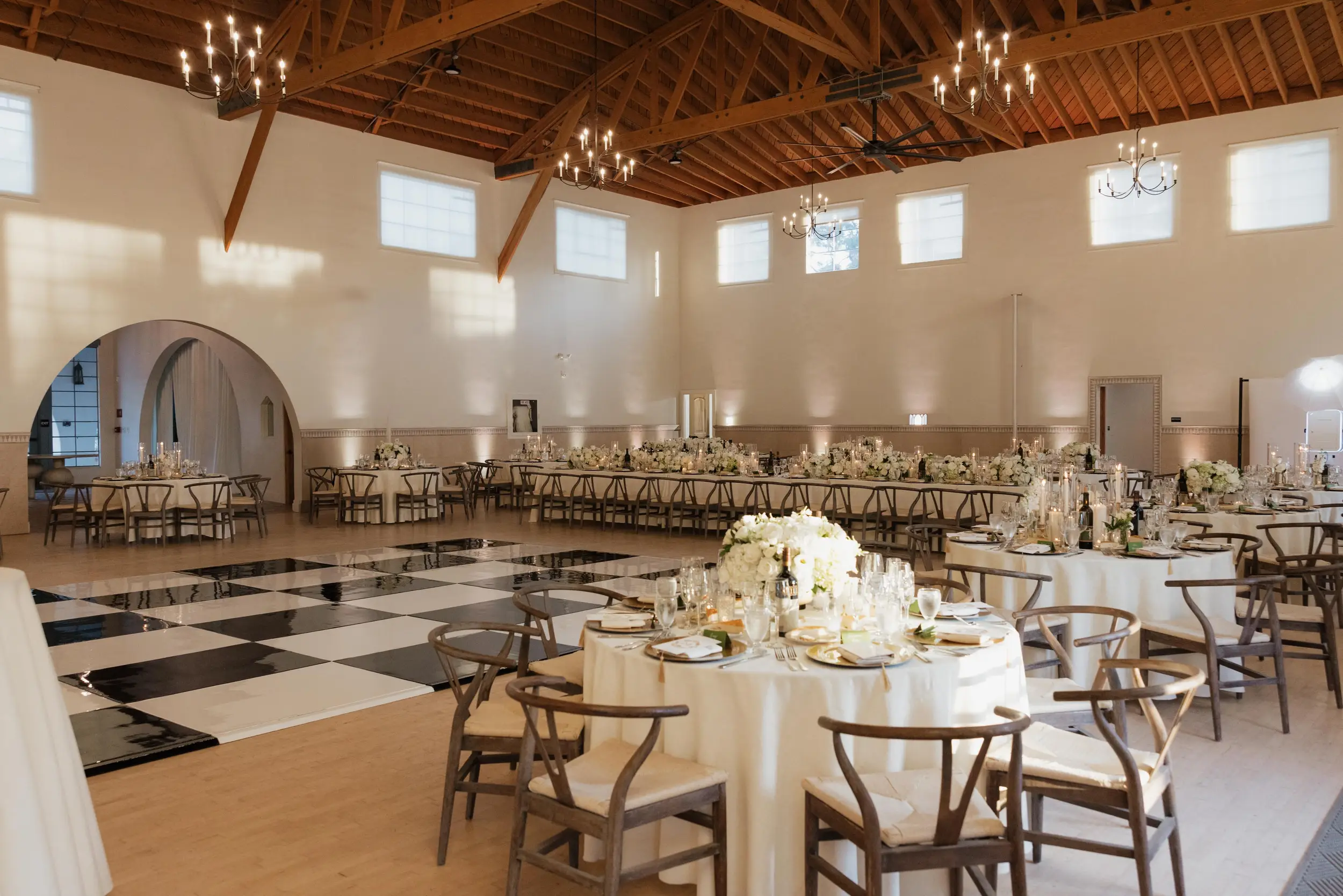 Reception tables topped with white florals surround a black and white checkered dance floor.